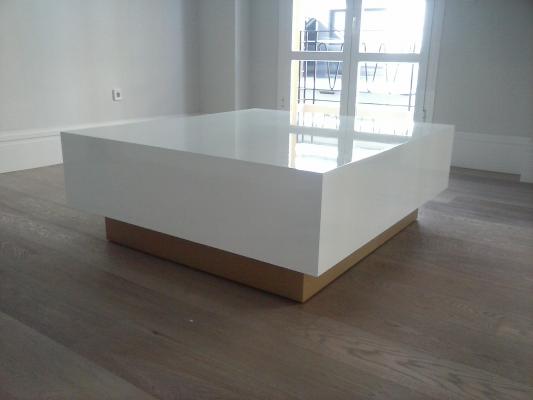Mesa de centro lacada en color blanco brillante y pie en color dorado.